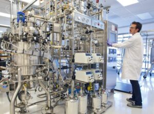 Researcher in a lab coat in front of a complicated stainless steel device.