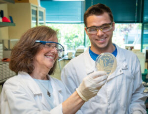 Two people in PPE smiling as they regard a petri dish.